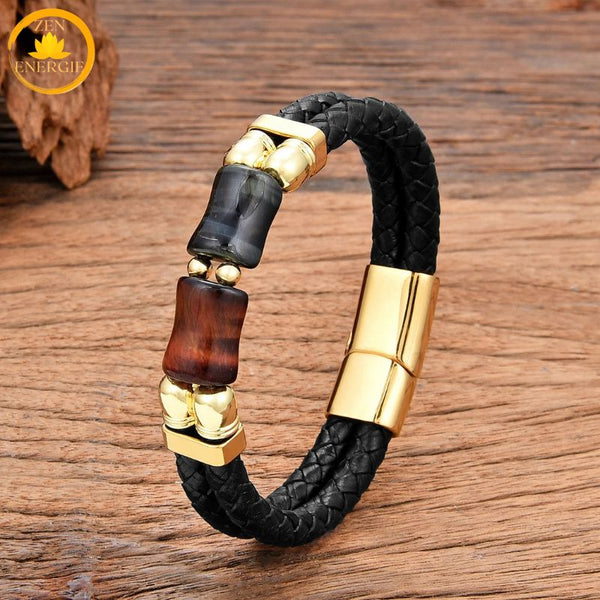 alt="Bracelet homme en cuir tressé noir avec pierres œil de faucon bleu-gris et œil de taureau rouge, fermoir doré"

