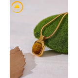 alt="Collier doré avec pendentif en pierre œil de tigre, bijou raffiné posé sur un support naturel"
